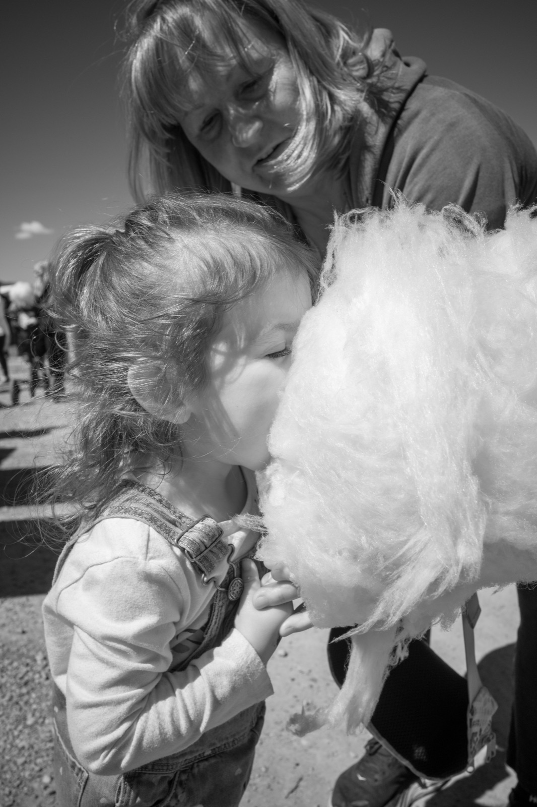A child and an adult share a cloud of cotton candy outdoors in black and white.